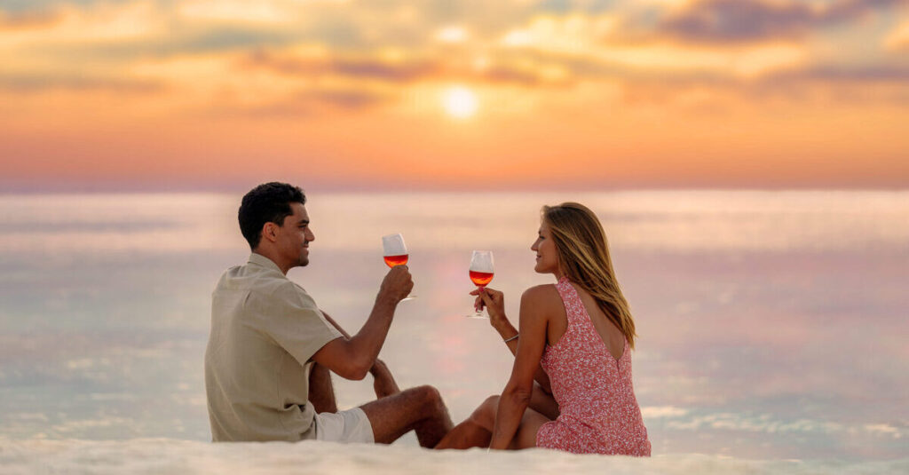 Una pareja brinda con vino en una playa de Maldivas durante la puesta de sol