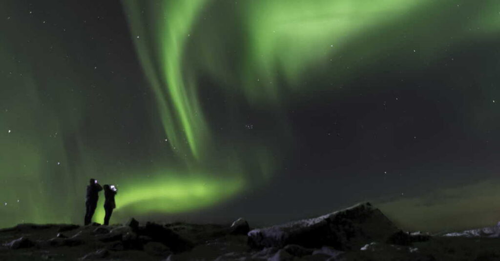 Dos persona captando el momento en el que aparecen auroras boreales en el cielo islandés